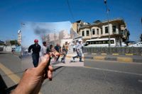 En man håller upp ett fotografi från ett attentat i Irak, 2005, på samma plats i mars 2023 – 20 år efter USA:s invasion.