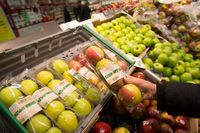 En kvinna väljer varor i frukt- och grönsaksdisken i en av Willys butiker. Ekologiskt odlade äpplen.