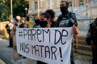 En demonstrant håller upp en banderoll med texten "sluta döda oss!" under en protest utanför delstatsregeringens högkvarter i Rio de Janeiro mot polisvåld mot svarta i söndags.