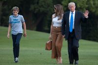 President Donald Trump vinkar när han går tillsammans med Melania och Barron utanför Vita huset i Washington.