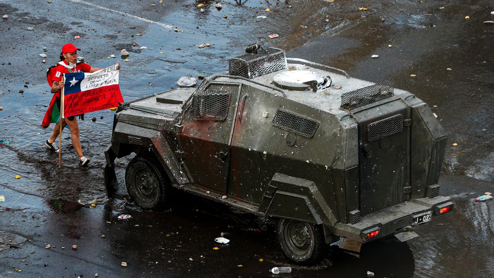 En aktivist håller i den chilenska flaggan framför en militär pansarvagn under en regimkritisk marsch i Santiago den 22 oktober.