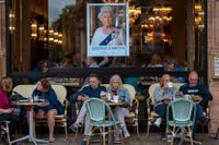 Turister på ett café i London under en bild av drottning Elizabeth.