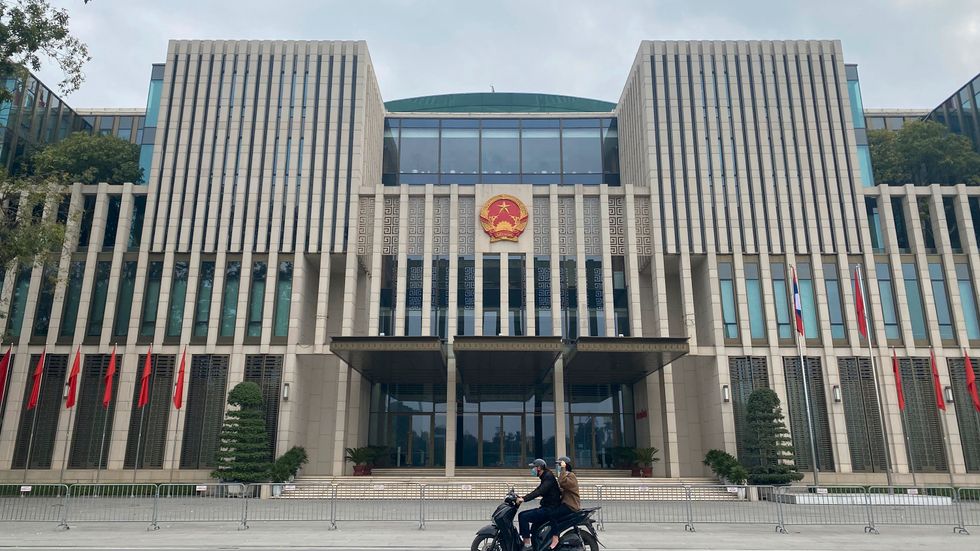 En mopedist med passagerare passerar nationalförsamlingen i Hanoi. Arkivbild.