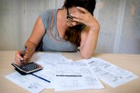 En skuldsatt kvinna sitter lutar över sina räkningar. Arkivbild.