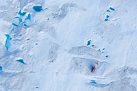 Forskare runt en helikopter, nere till höger i bild, på den grönländska Helheim-glaciären. Fotot togs 2019, då instrument sattes upp på glaciären för att mäta hur snabbt den smälter.