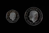Två av de nya mynten med kung Charles III. Till vänster ett 50 pencemynt och till höger specialmyntet på fem pund.