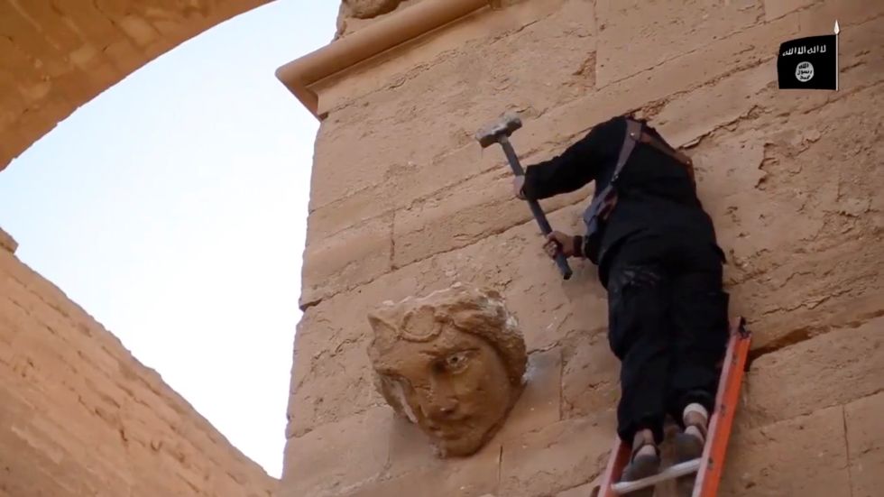 Företrädare för IS hugger ner ett väggmonument i Hatra i Irak 2015. Terrororganisationen tjänade stora pengar på plundring och smuggling av kulturarvet i Syrien och Irak. 