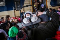 En man bär ett barn då människor försöker ta sig ombord på ett tåg på stationen i Kiev.