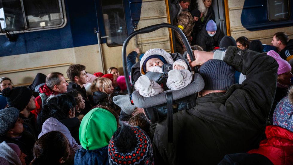 En man bär ett barn då människor försöker ta sig ombord på ett tåg på stationen i Kiev.