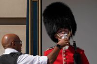 En polis ger vatten till en soldat i vaktstyrkan utanför Buckingham Palace i London på måndagen.
