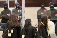 Försvarsadvokaterna talar med de åtalade inför rättegångsstarten i Bryssel, med maskerad polis i bakgrunden.