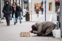 En person tigger på gatan i Stockholm. På en handskriven lapp vädjas om hjälp med pengar till mat.