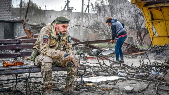 En ukrainsk soldat sitter på en bänk i Orichiv och röker. I bakgrunden städas rasmassor och bråte undan efter ett ryskt anfall från luften. Bilden togs den 5 april.