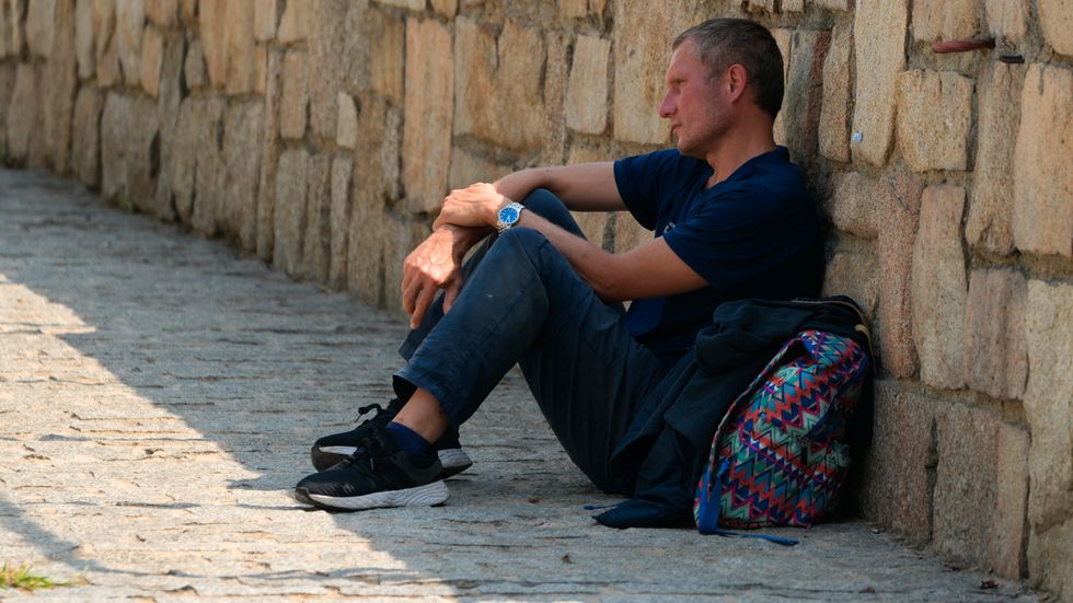 En man vilar i skuggan vid en stenmur i Madrid i juli. Arkivbild.