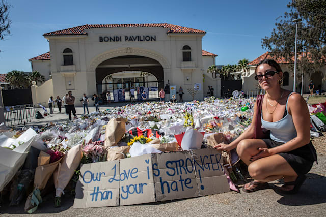 Bondibon Chloe places a homemade sign at the memorial site on Bondi Beach.