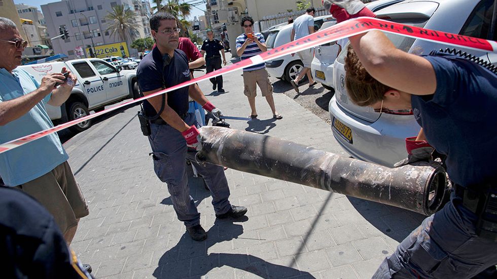 Israeliska militära experter bär iväg resterna av en raket som skjutits från Gaza den 11 juli i år. Raketen träffades av en israelisk anti-missil, men landade trots det på en synagoga i Tel Aviv.