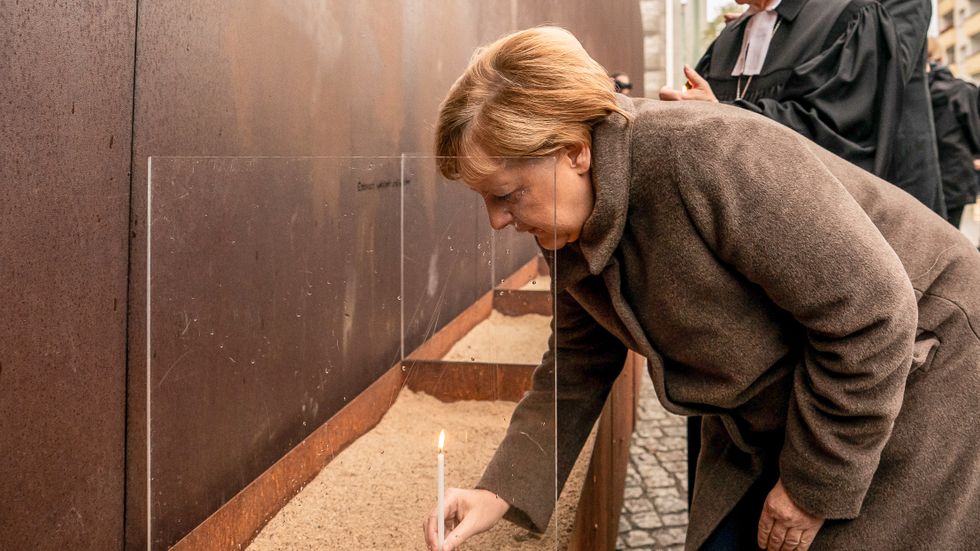 Angela Merkel tänder ett ljus vid ett stycke av Berlinmuren som står kvar.