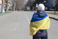 En kvinna med den ukrainska flaggan står framför ryska trupper i Cherson i mars i år. Nu riktar Ukraina fokus på att återta staden.