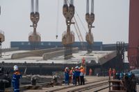 Den stora brokonstruktionen lyfts till pontonerna i hamnen i den kinesiska staden Zhongshan för att sedan avgå mot Stockholm.