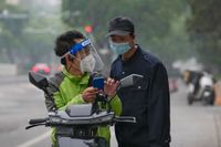 Ett varubud i Shanghai med andningsskydd och visir frågar en säkerhetsvakt om vägbeskrivning. Fotot är taget den 10 maj.