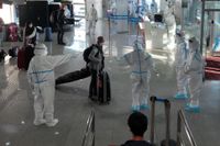 Skyddsklädd personal tar emot de anländande på flygplatsen i Peking.