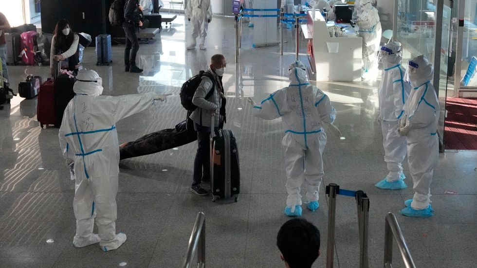 Skyddsklädd personal tar emot de anländande på flygplatsen i Peking.