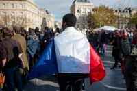 En man har lindat en fransk flagga runt sig under en nationell tyst minut för att hedra offren i fredagens terrorattacker.