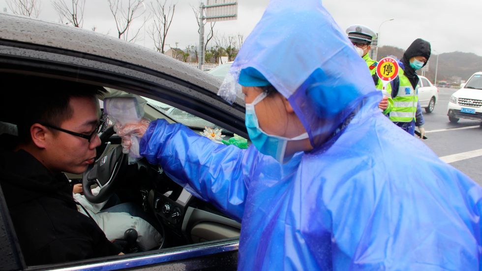 Kontrollant tar temperaturen på resenärer på väg in i Wenling i Kina i ett försök att hejda spridningen av coronaviruset.