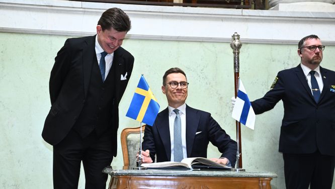 Talman Andreas Norlén tittar på när Finlands president Alexander Stubb skriver i riksdagens gästbok.