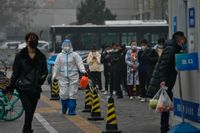 En anställd i skyddsdräkt sprejar desinfektionsmedel medan Pekingbor köar för att testa sig för covid-19.