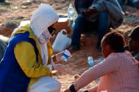 Överlevande från katastrofen utanför al-Khums får hjälp en IOM-medarbetare på stranden på torsdagen.