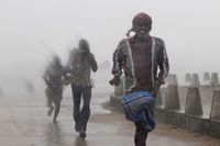 Människor springer för att söka skydd från regn och hårda vindar vid kusten i Gopalpur, Orissa.
