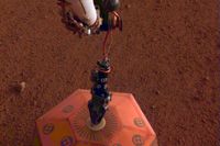 Bild från Nasa som visar hur Insights arm ställer ner seismometern på Mars yta. Det franskbyggda instrumentet är klätt i koppar, som glimmar i Marssolen.