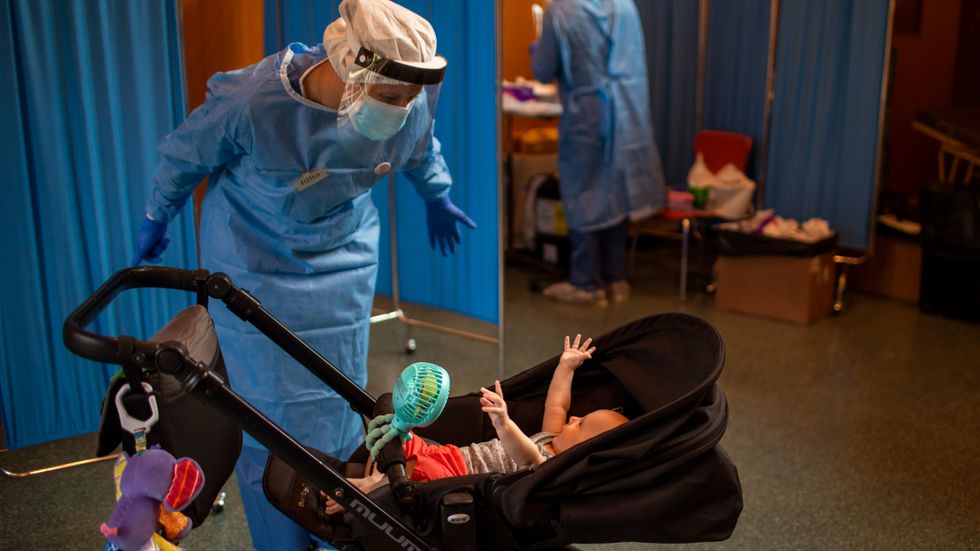 En vårdarbetare leker med en bebis medan barnets pappa gör ett coronatest i Barcelona.