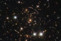 Bilden visar galaxklustret 4,6 miljarder ljusår bort. Längsmed syns fyra korta bågar – tre uppe till höger, en nere till vänster – från galaxen Sunburst arc, som ligger 11 miljarder ljusår bort.