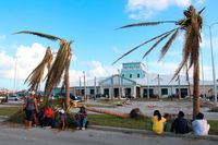 Folk sitter mellan sönderslitna palmer utanför Marsh Harbours flygplats i norra Bahamas.