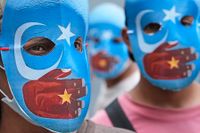 Demonstranter mot behandlingen av uigurerna bär masker med den östturkestanska flaggan som tystas av en kinesisk hand.