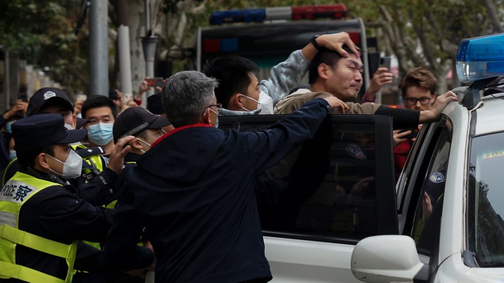 En man tvingas in i en polisbil under protesterna i Shanghai, Kina, söndagen den 27 november. 