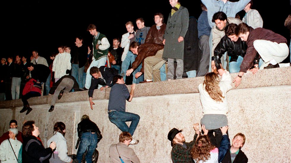 Östtyska medborgare klättrar över Berlinmuren efter att gränsen öppnats i november 1989.