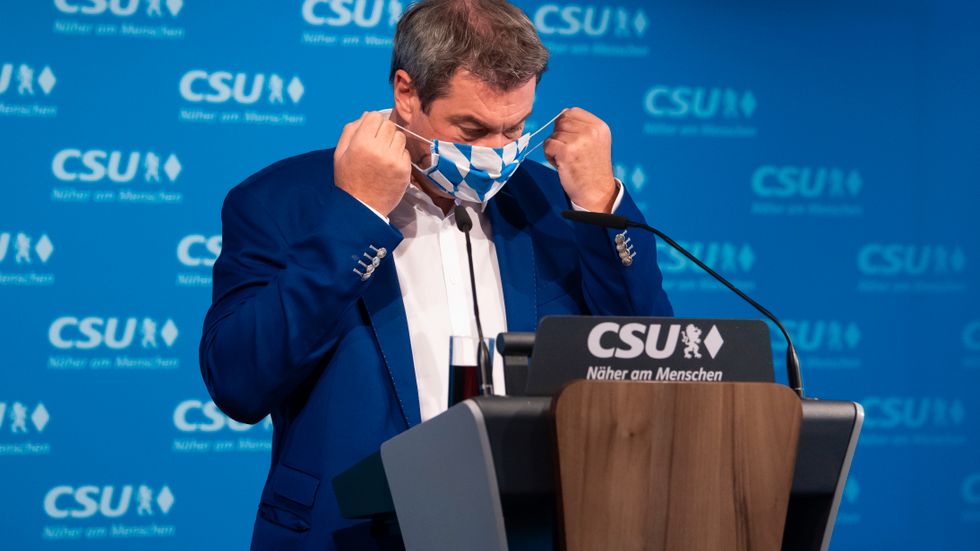 Bayerns ministerpresident Markus Söder tar av sig munskyddet inför en presskonferens i München.