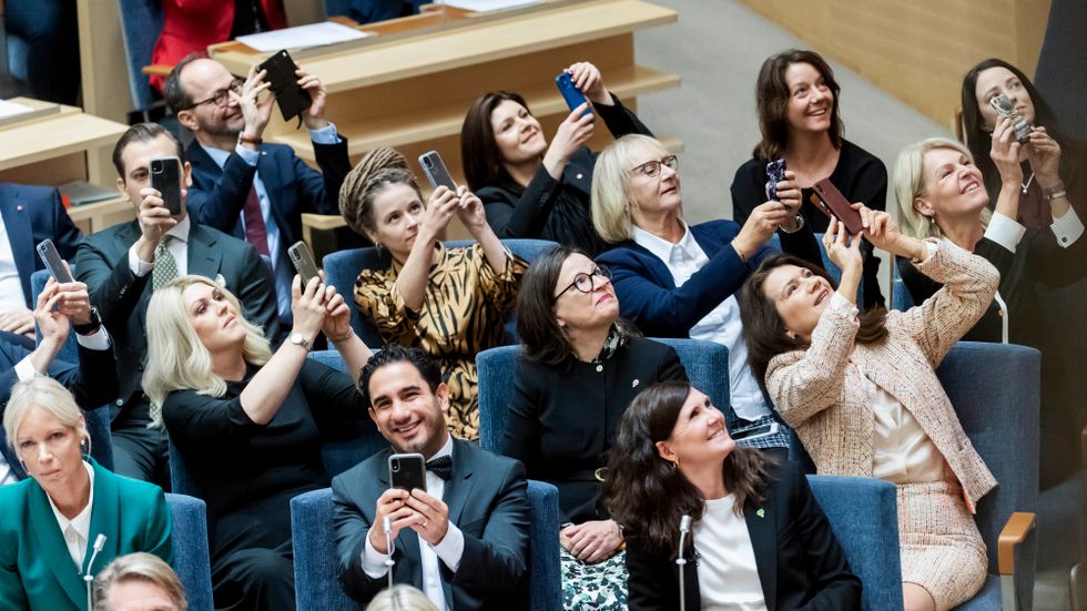 Statsrådens ansikten och mobilkameror vänds mot skärmen som visar att Sveriges första kvinnliga statsminister är vald. 