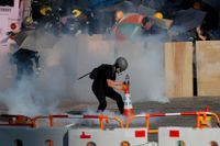 En demonstraadmnt försöker kväva en tårgasbehållare under måndagens generalstrejk i Hongkong.