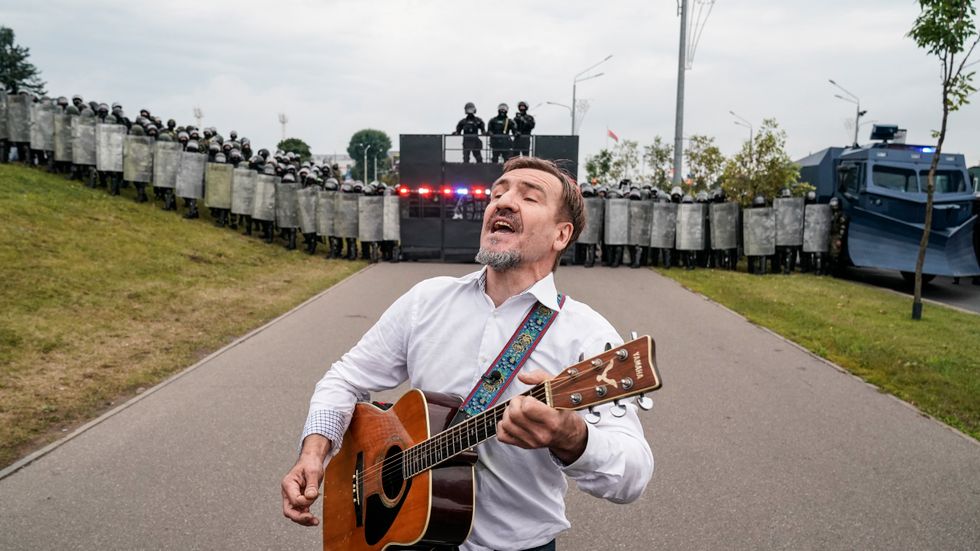 En man spelar gitarr framför kravallpolis i Belarus.