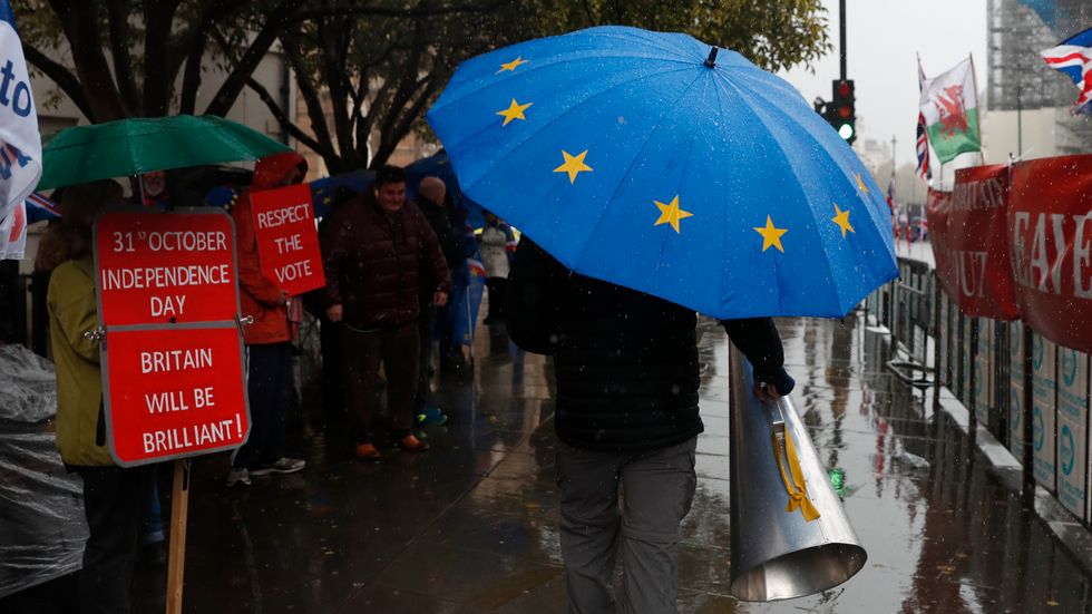 Anti-Brexiteer Steve Bray carries his megaphone past pro Brexit supporters as they shelter from the heavy rain outside the Houses of Parliament in London, Thursday, Oct. 17, 2019. 