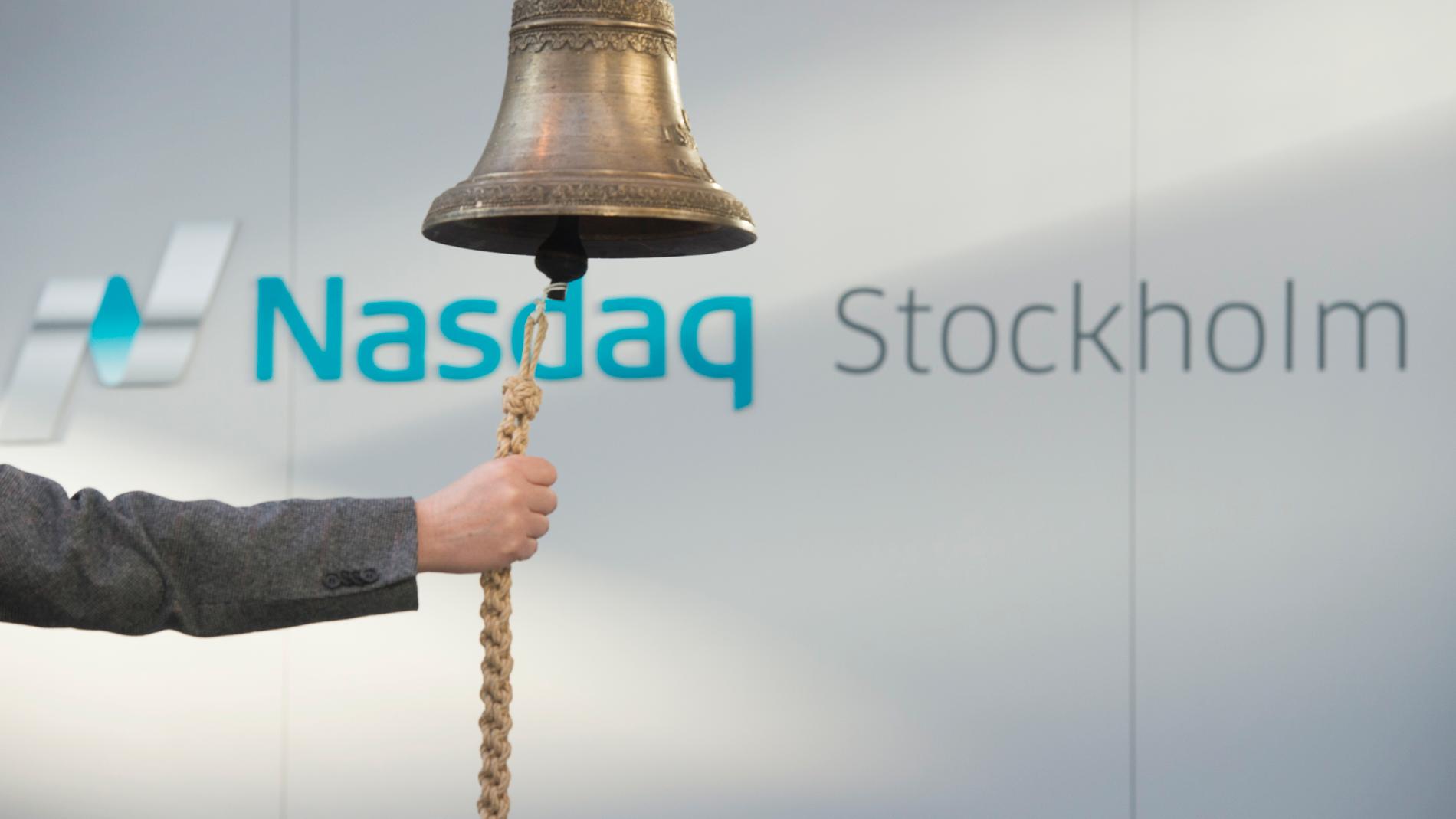 En ringklocka framför Nasdaq Stockholms logotyp