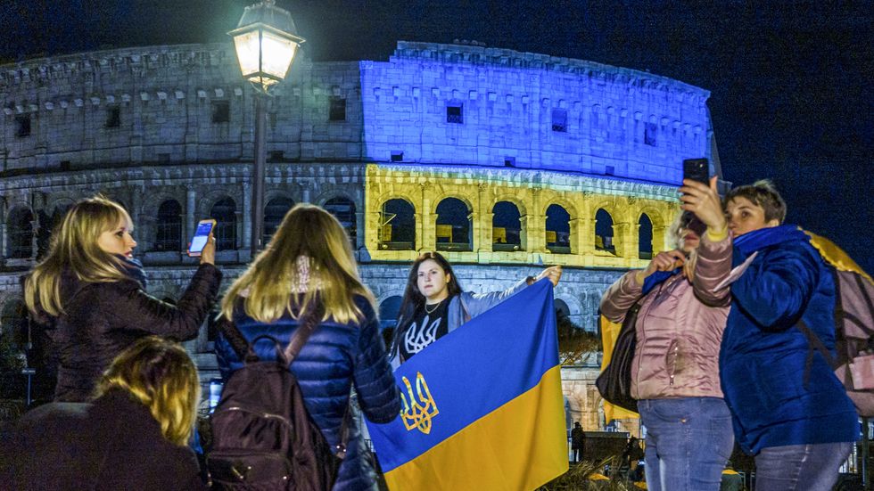 Människor samlade vid Colosseum i Rom som är upplyst i blått och gult till stöd för Ukraina.