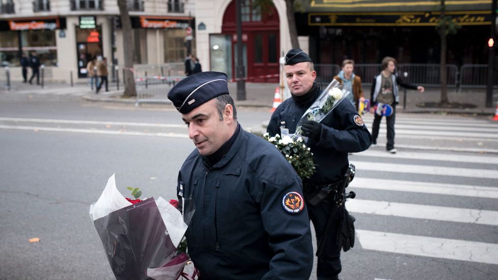 Franska poliser med blommor de har fått av människor utanför konsertlokalen Bataclan i Paris.