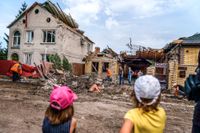 Barn ser på när räddningsarbetare rensar upp vid ett förstört hus i Kramatorsk i östra Ukraina, 12 augusti 2022.