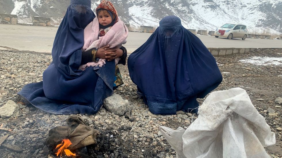 Två kvinnor och en 1,5 år gammal pojke värmer sig vid en brasa i östra Afghanistan i januari 2022.