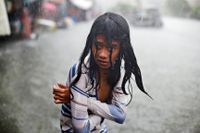 En flicka försöker hålla sig varm nära Manila i Filippinerna under ett kraftigt oväder sommaren 2015.